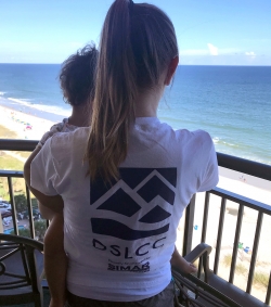 Lady holding child at the shore with DSLCC logo'd shirt on